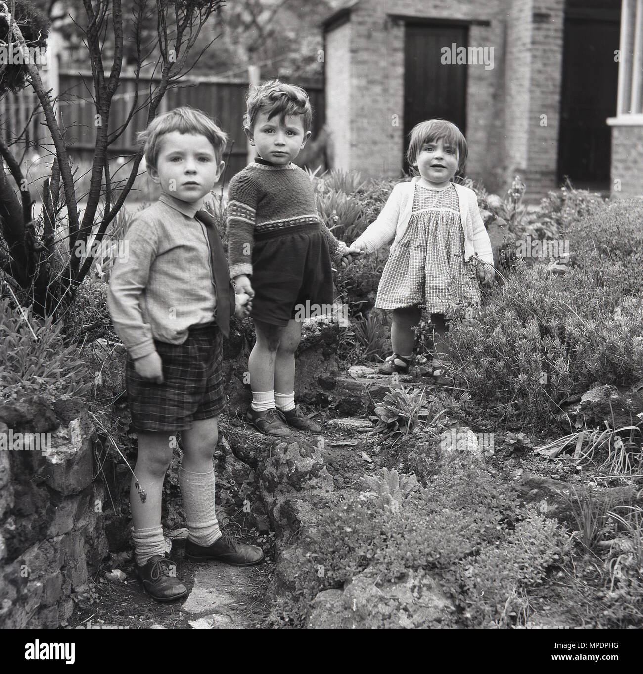 1961, historische, drei Kinder halten Hände beim Spielen im Steingarten