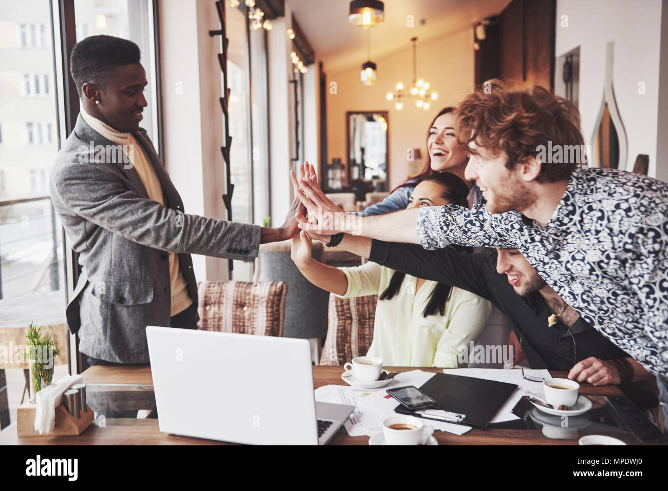 Glückliche junge Unternehmer in Freizeitkleidung im Cafe Tabelle oder im Business Office geben High Fives zu einander, als ob Erfolge feiern oder Starten neues Projekt Stockfoto