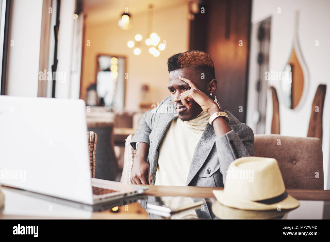 Nachdenklich, afro-amerikanische stattlichen professioneller Schriftsteller der beliebtesten Artikel im Blog im trendigen Outfit gekleidet und Gläser denken über neue Geschichte Korrekturlesen sein Skript von Notebook im Cafe sitzen Stockfoto