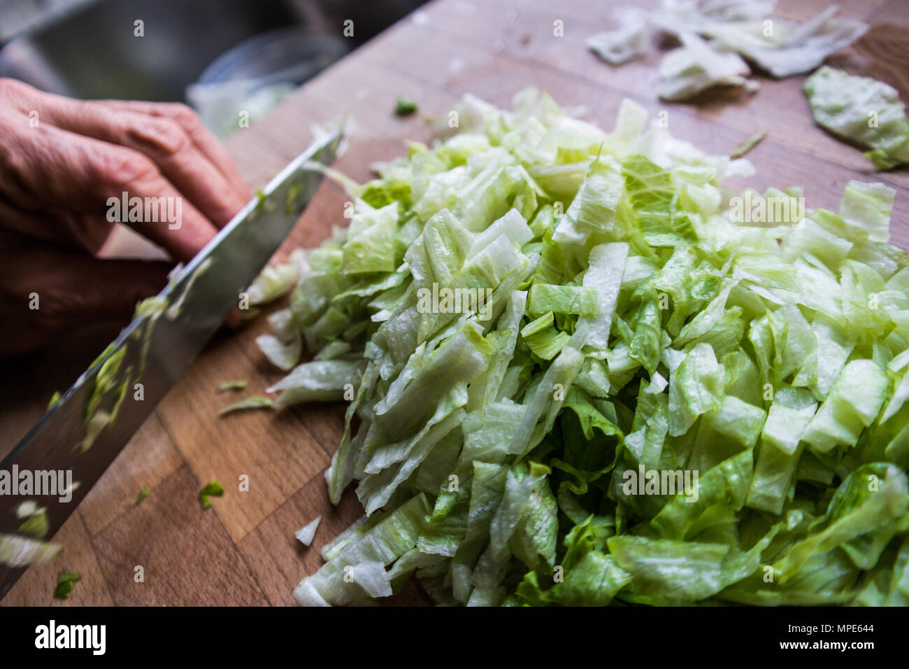 Frau hacken Salat mit messer an holz- Oberfläche Stockfoto