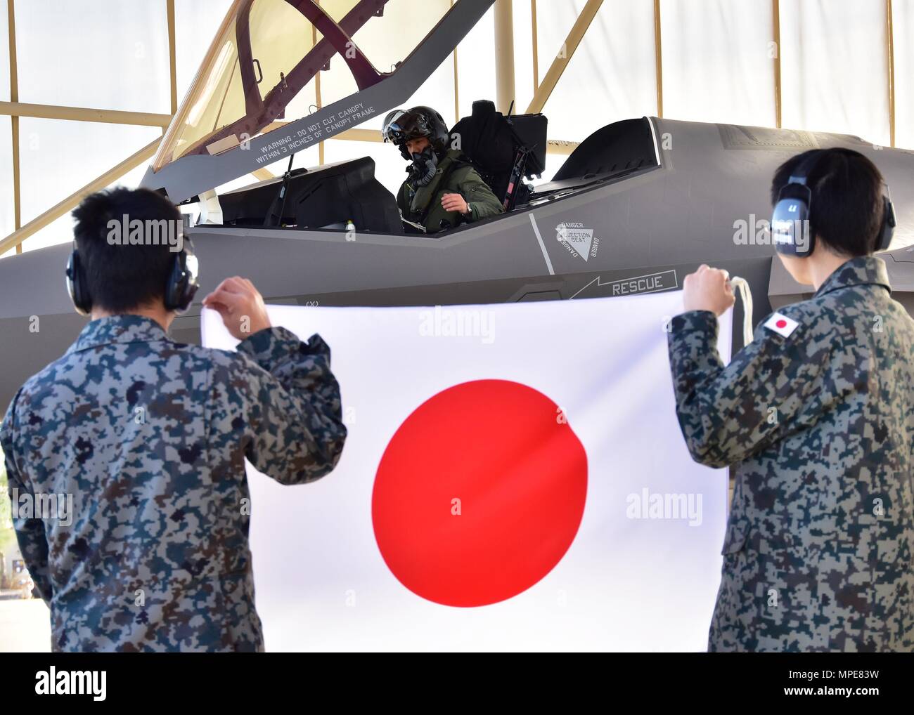 Oberstleutnant Nakano, Japan Air Verteidigung-kraft F-35 einen nationalen Vertreter Pilot zu Luke, sitzt im Cockpit eines der drei F-35s auf der Rampe, die 944th Fighter Wing Feb 7 vor der Abreise während zwei jasdf Betreuer ein Japan Flagge oben an Luke Air Force Base, Ariz (USA halten Air Force Foto von Tech. Sgt. Louis Vega Jr.) Stockfoto