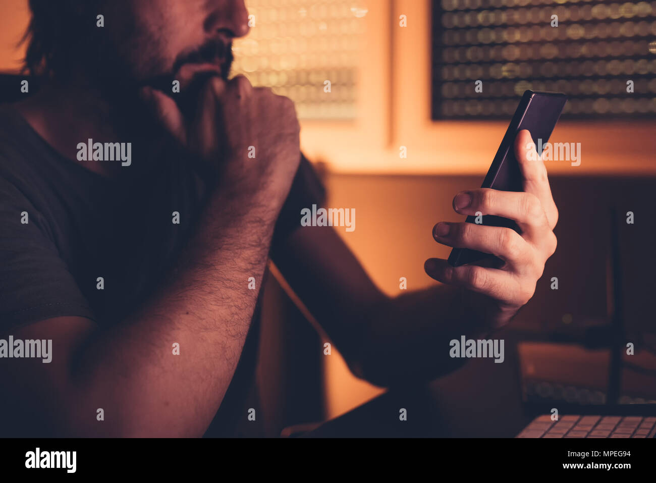 Mann mit Smart Phone im Home Office. Freelancer mit Handy für die Kommunikation wie SMS, Chat Apps oder e-mail beantworten. Low Key mit Stockfoto