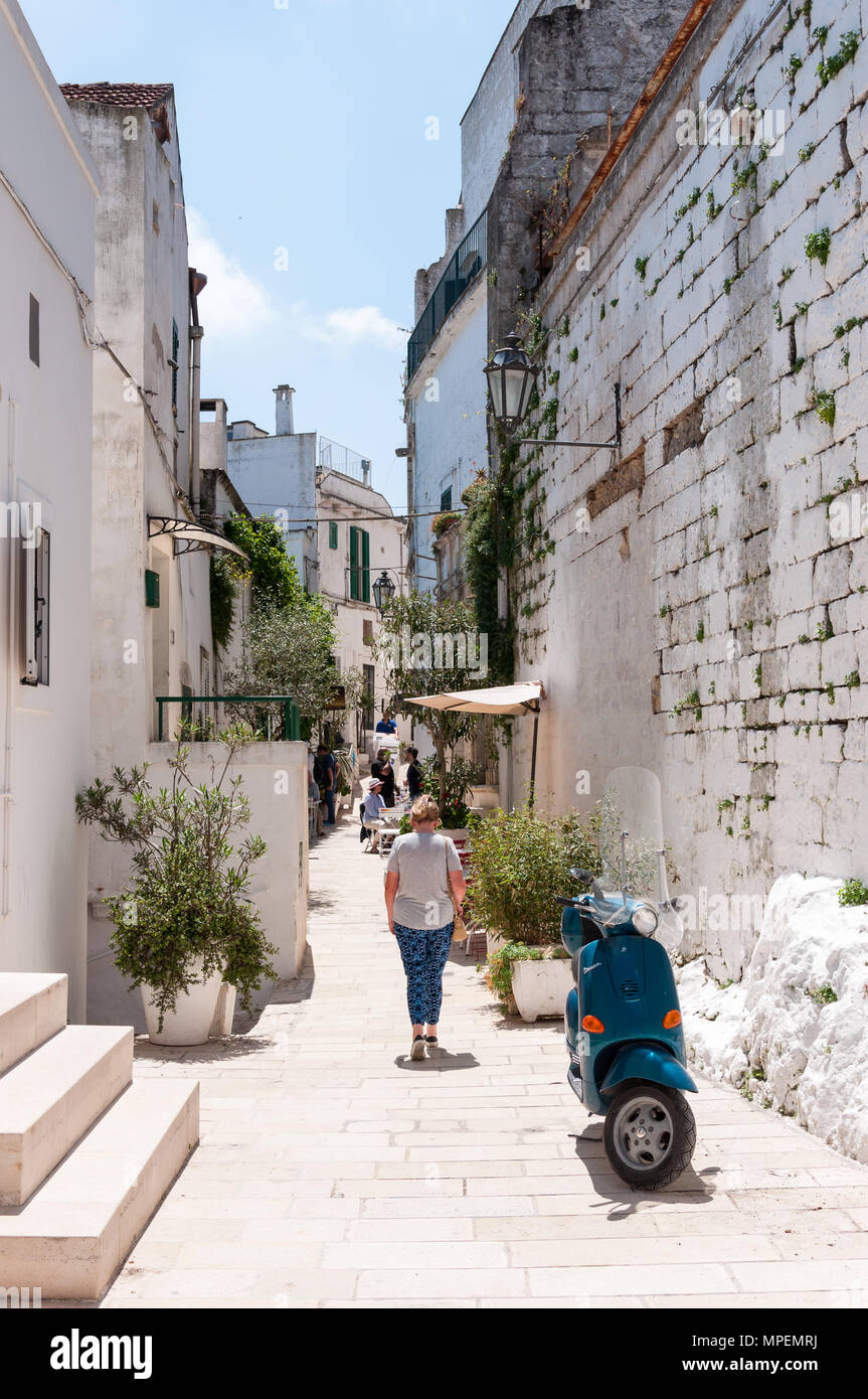 Touristen in einer engen Straße in der Altstadt von Ostuni, in Apulien, Süditalien. Einen geparkten blauen Motorroller im Vordergrund. Stockfoto