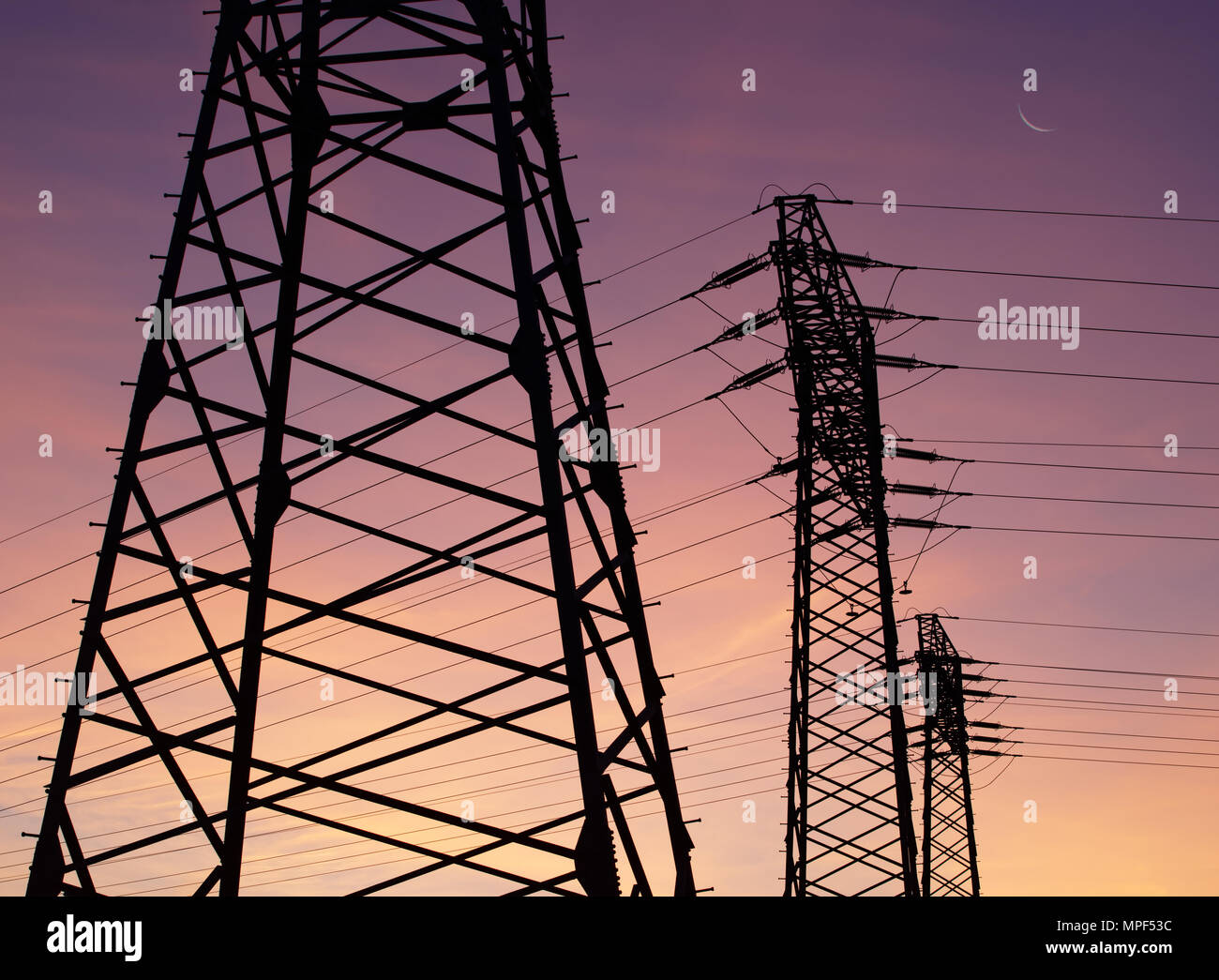 Drei Strommasten mit Kabel sind gestaffelt als Silhouetten vor einer farbigen Abendhimmel. Der Mond als schmale Sichel zu sehen. Stockfoto