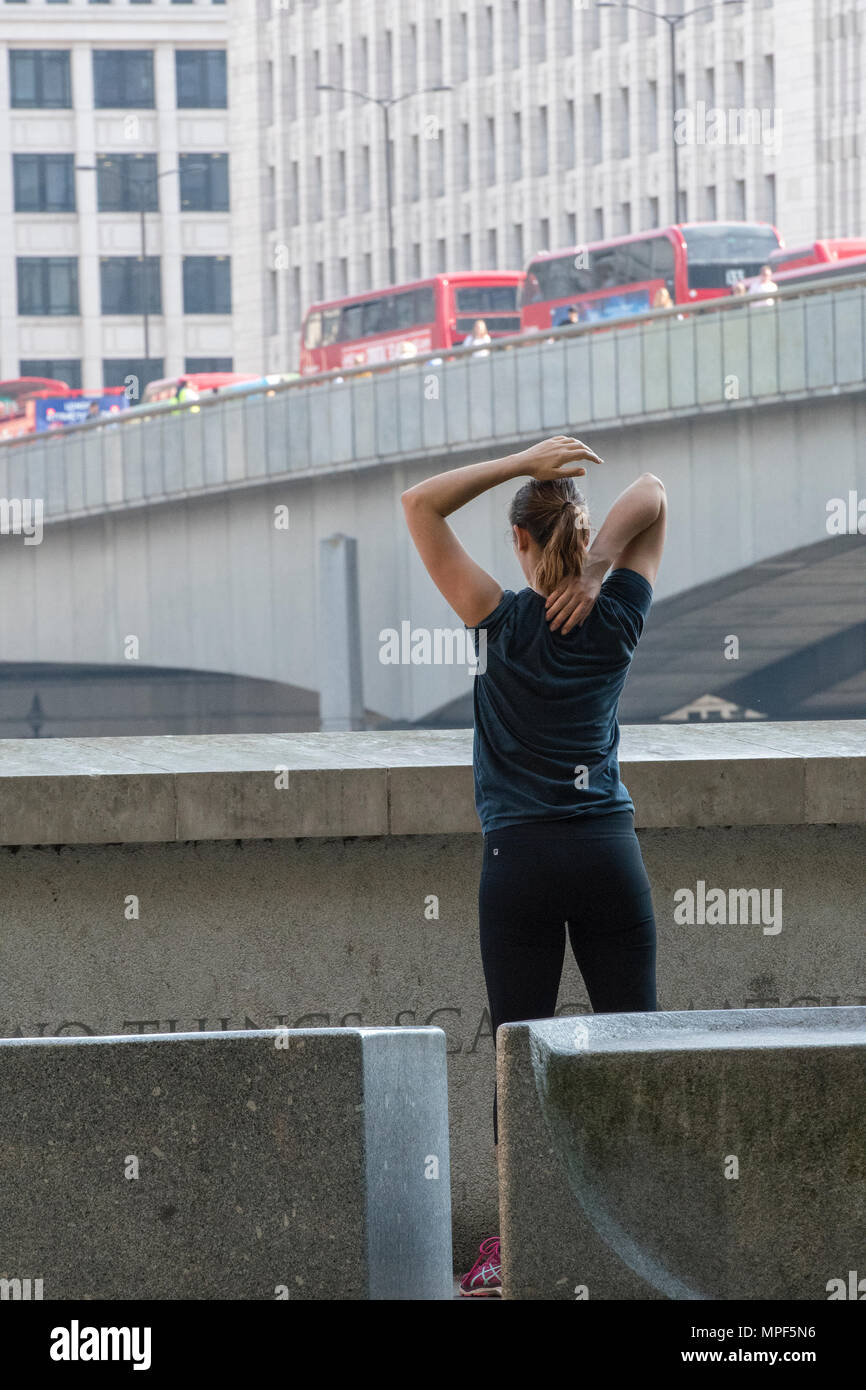 Eine junge Frau, die Ausübung oder Wahrnehmung während der morgendlichen Rush hour in Central London. Stretching Übungen die Muskulatur zu lockern nach der Ausführung. Stockfoto
