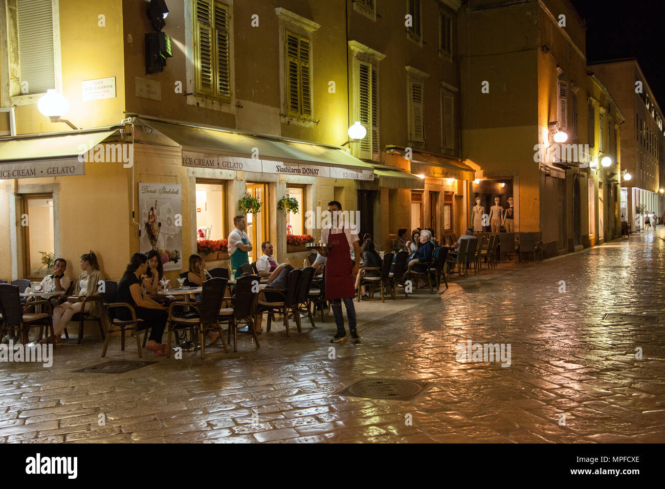 Nachts beleuchtete Straße Szene von Menschen Essen und Trinken im Freien an einem Bordstein, Restaurant Cafe im kroatischen Hafen von Zadar Kroatien Stockfoto