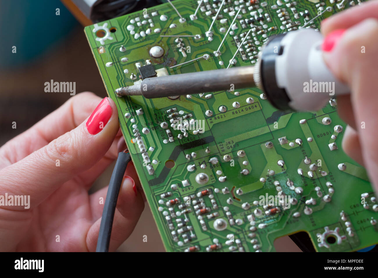 Das Mädchen - Techniker repariert ein Schaltnetzteil. Installation und Löten von elektronischen Bauteilen mit einem Lötkolben mit einem keramischen Heizelement. Stockfoto