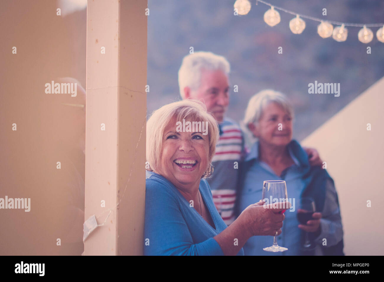 Großes Lächeln für gealterte Frau während der Freizeitaktivitäten auf der Terrasse bei Nacht. Trinken Wein und Spaß an der Party mit Freunden Senior Stockfoto