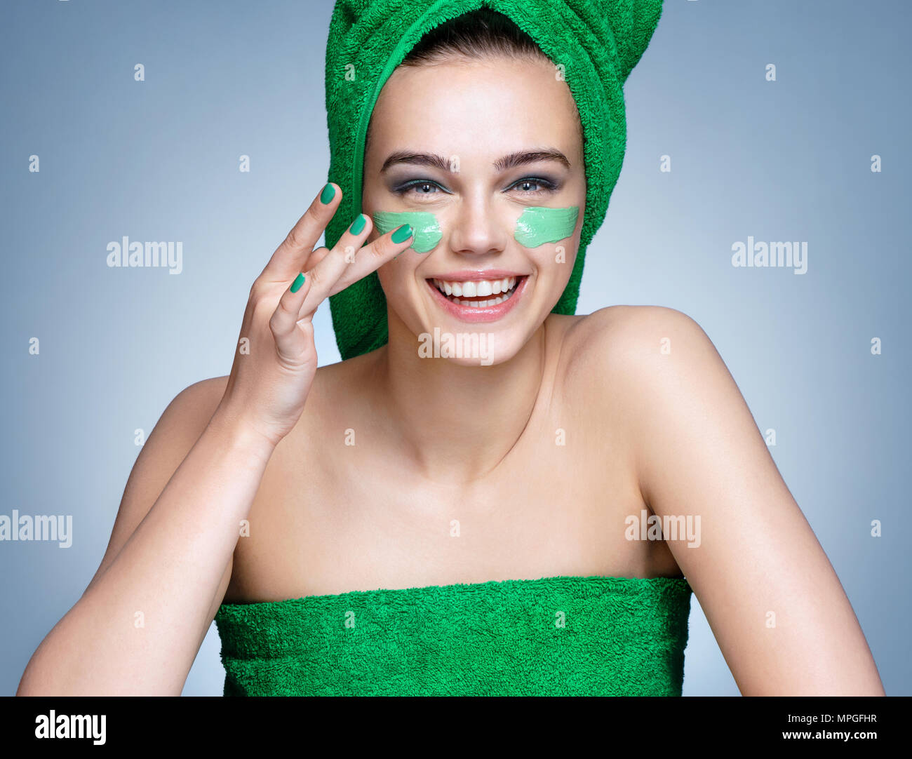 Lachende Mädchen in grün Bettwäsche anwenden, feuchtigkeitsspendende Creme im Gesicht. Foto von Mädchen mit makelloser Haut auf blauem Hintergrund. Hautpflege und Schönheit conce Stockfoto