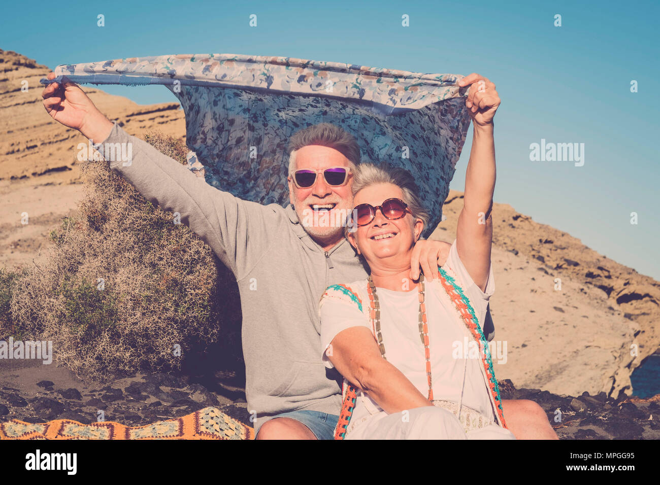 Rentner und Ferienhäuser Freiheit Konzept für hippy senior Paar Mann und Frau spielen mit dem Wind mit farbigen clotehs. Einrichtung in Pastelltönen und blauer Himmel für s Stockfoto