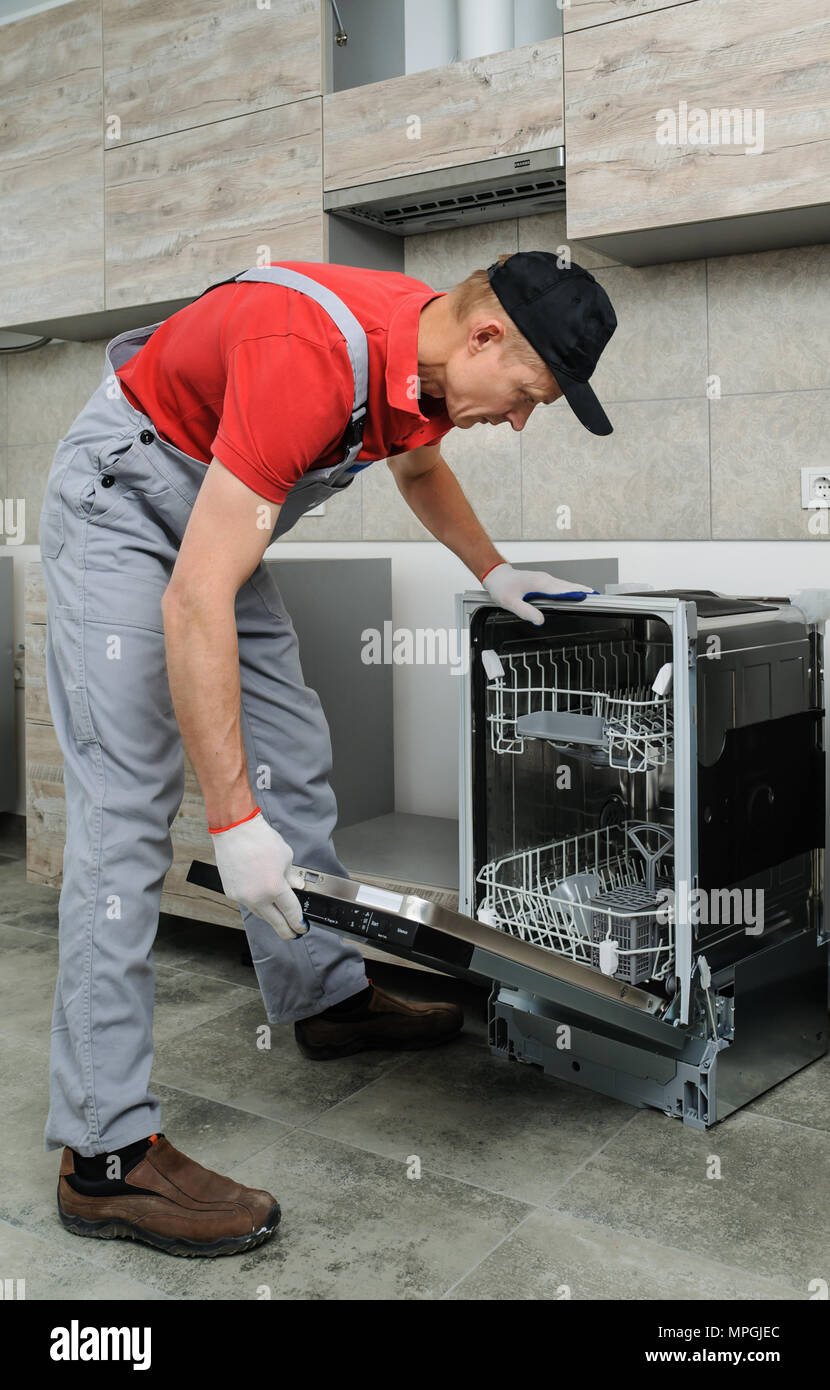 Installation der Küche. Der Arbeiter stellt den Geschirrspüler an seinen Platz. Stockfoto