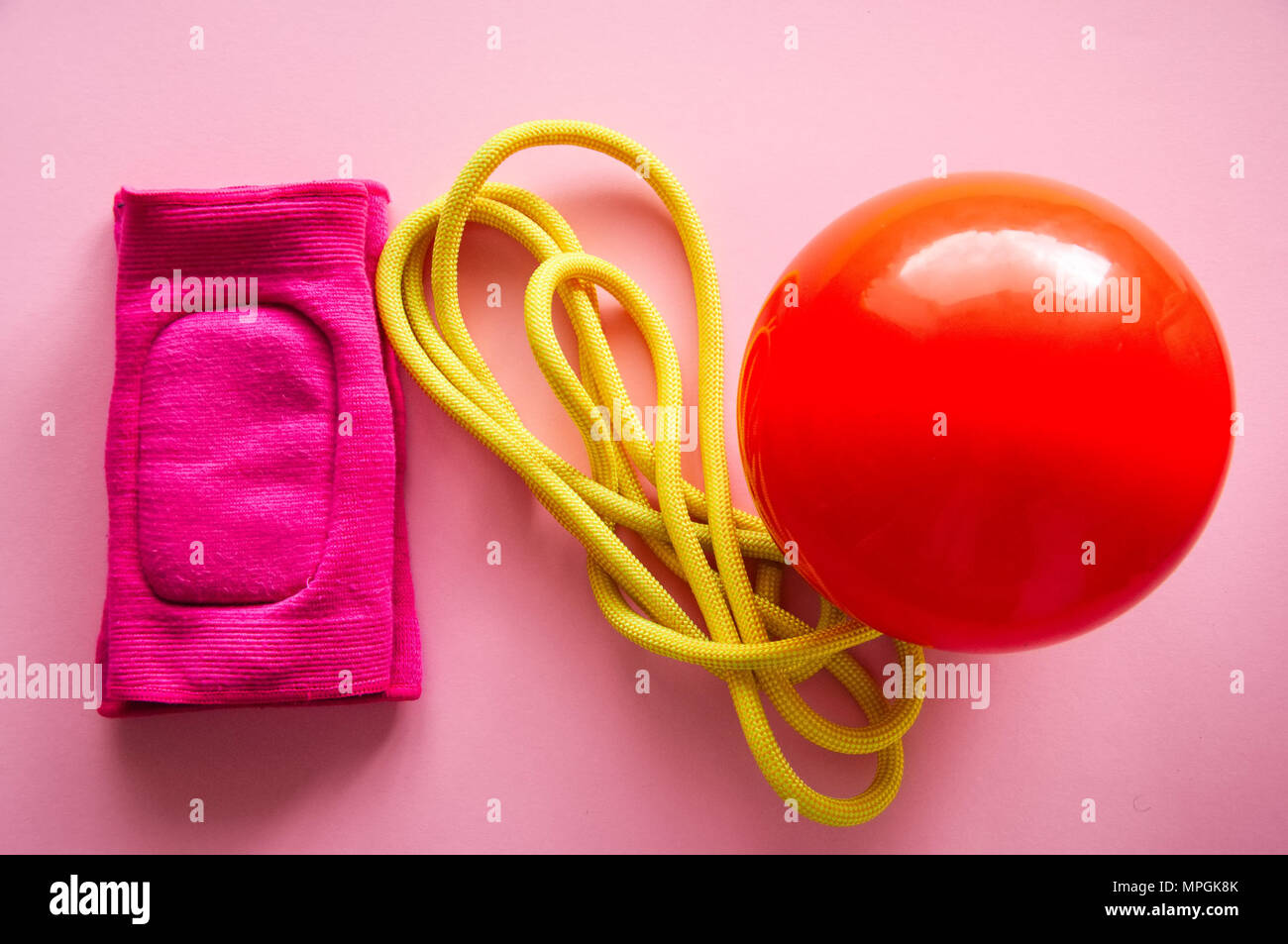 Rot Gymnastikball, Knieschoner und Springseil auf einem rosa Hintergrund. Sport, Hobby und Lifestyle Konzept. Ansicht von oben. Stockfoto