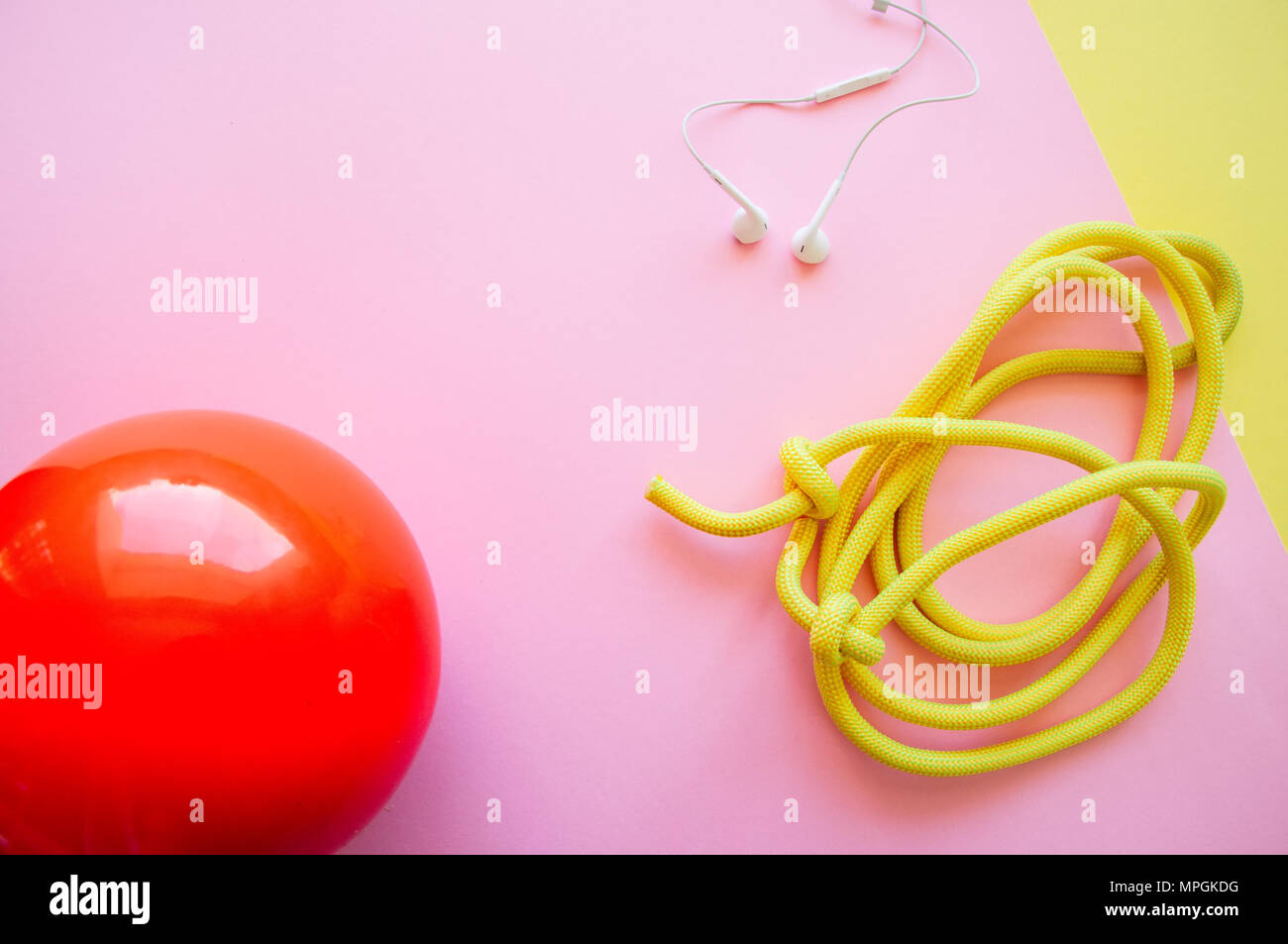 Rot Gymnastikball, Kopfhörer und Springseil auf einem rosa und gelben Hintergrund. Sport, Hobby und Lifestyle Konzept. Top ansehen und kopieren. Stockfoto