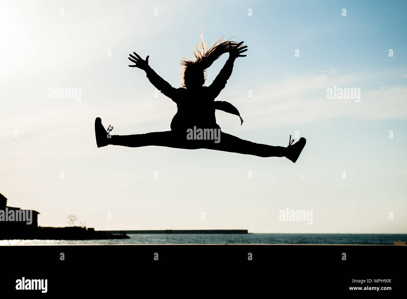 Silhouette von gesunden jungen Mädchen springen hoch in der Luft in der Stadt mit Blick auf das Meer im Sommer im Freien Stockfoto