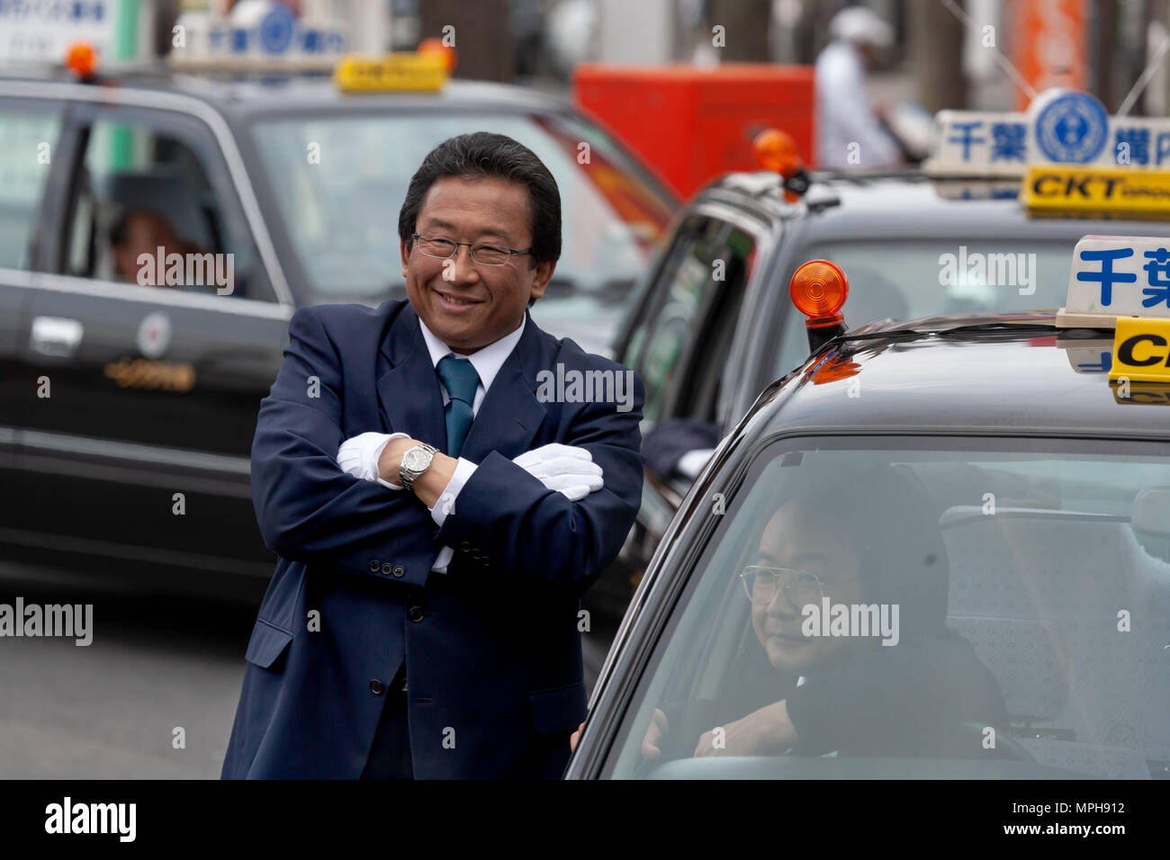 Japanische Taxifahrer neben 3 Taxis, die Arme verschränkt, Warten auf Passagiere in Tokio Stockfoto