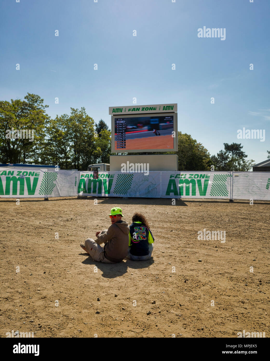19./20. Mai 2018. Le Mans, Frankreich. Hinter die Kulissen der MotoGP. Ein junges Paar sitzen auf dem Boden Schmutz den Trainings zu beobachten Auf einer der großen Leinwände. Stockfoto