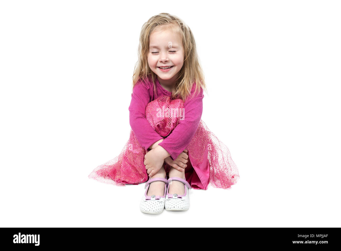 Porträt eines kleinen, schönen, lächelnde Mädchen mit geschlossenen Augen sitzen auf dem Boden und die Knie auf einem weißen Hintergrund isoliert umarmen Stockfoto