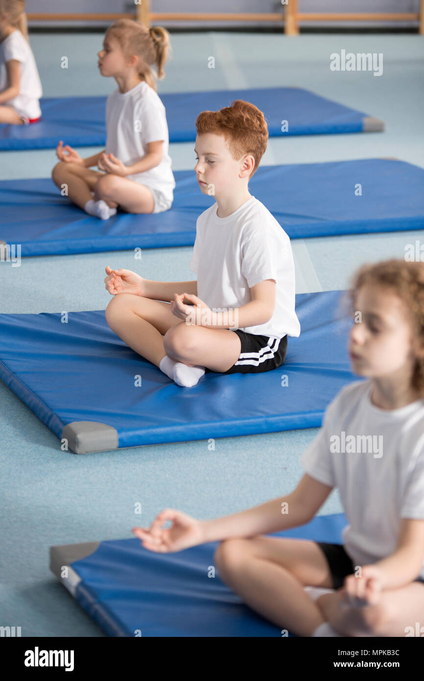 Grundschule Schüler und andere Kinder sitzen auf Matten mit gekreuzten Beinen und Augen in entspannenden Meditation Klasse geschlossen Stockfoto