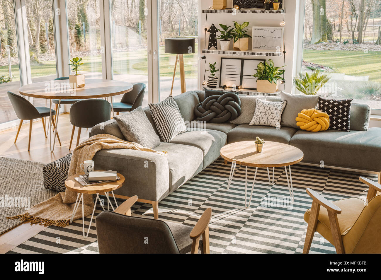 Hohe Betrachtungswinkel und eine stilvolle, nordic Wohnzimmer mit einem Esstisch aus Holz, grau Sofa und Blick auf Terrasse und Garten. Real Photo Stockfoto