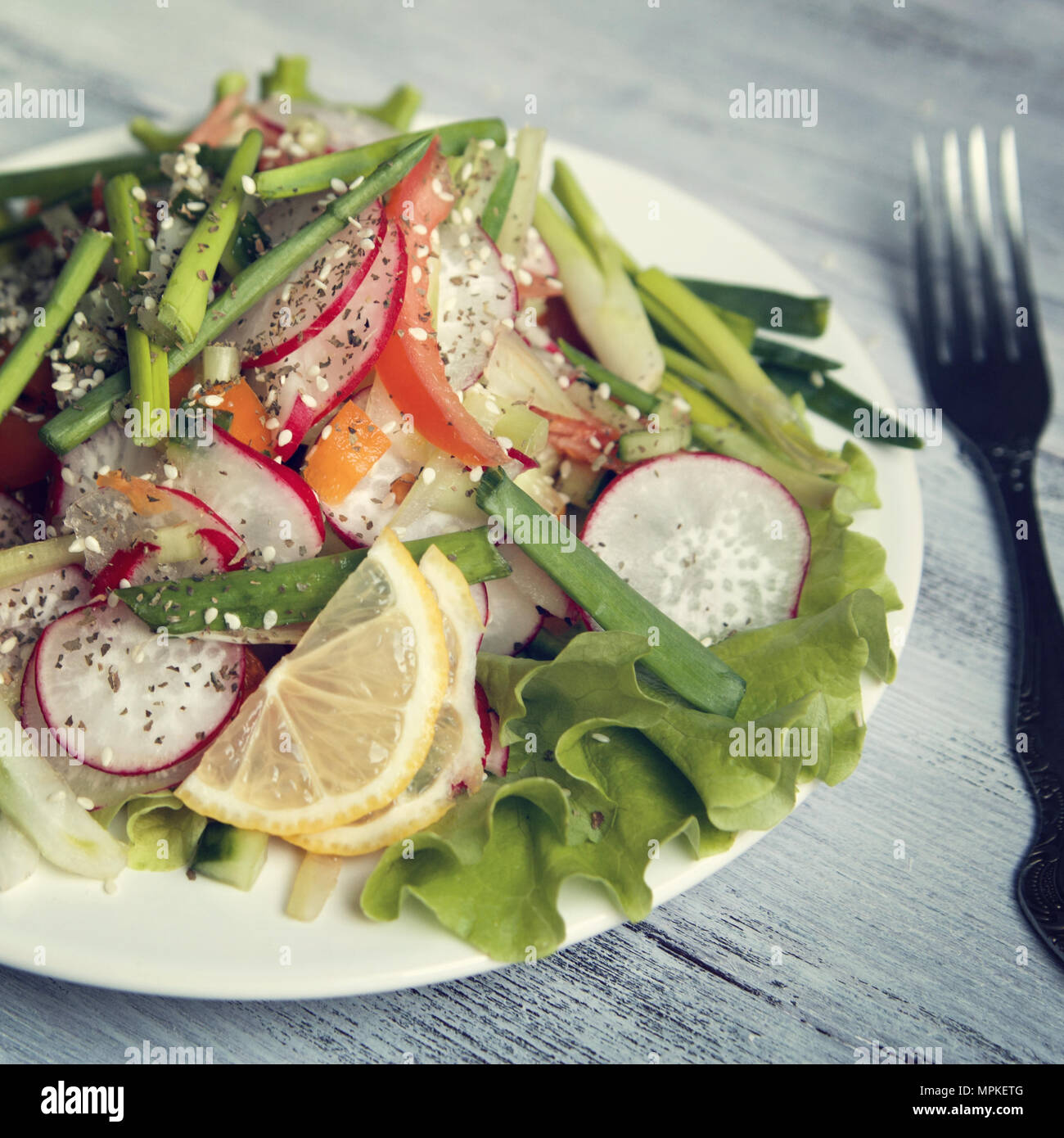 Frühjahr Salat auf dem weißen Teller. Rettich, Tomaten, Sellerie und Gurke. Mit Sesam gekrönt. Vegetarisches Gericht auf die weiße Holztisch. C Stockfoto