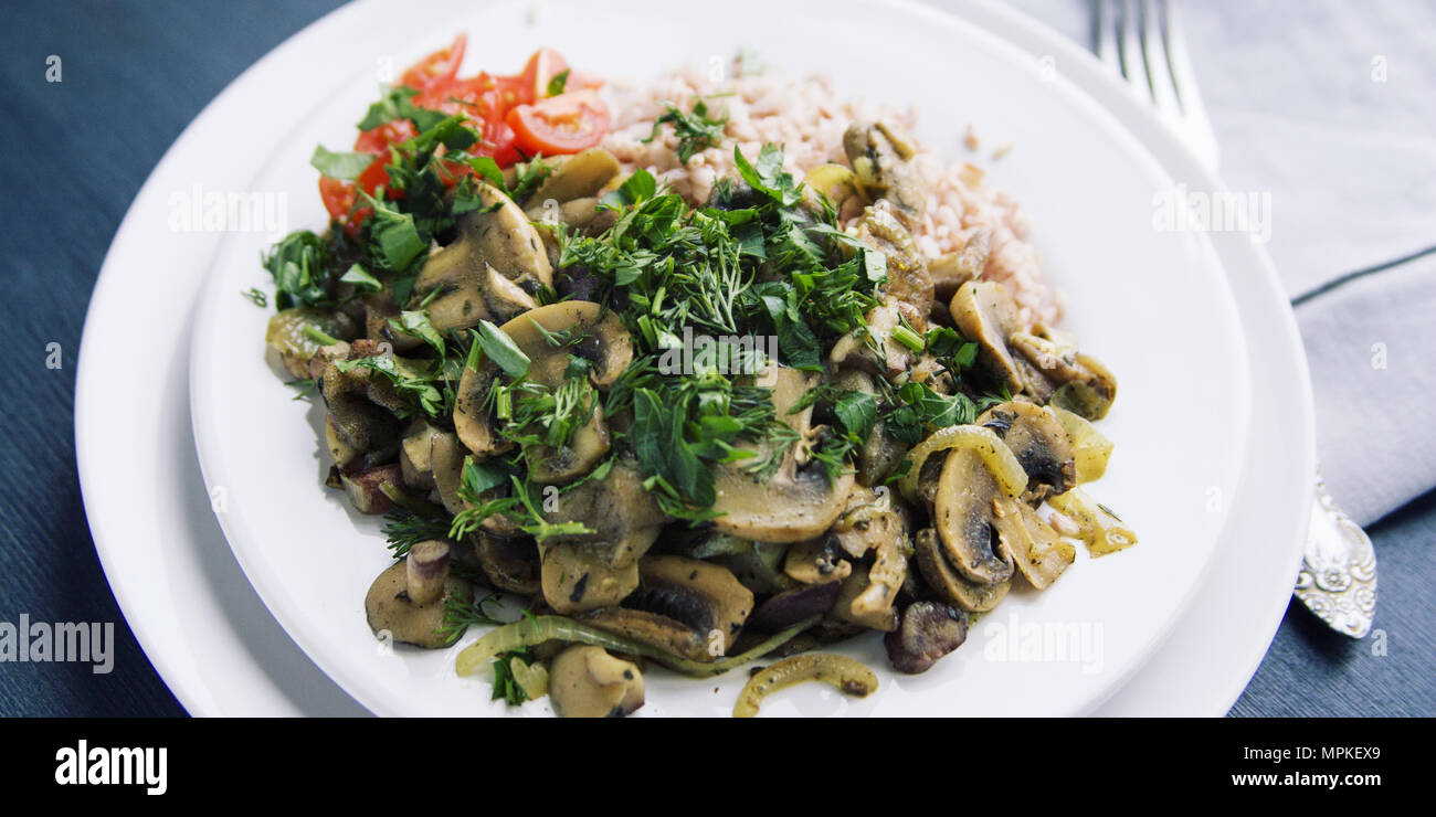 Roter Reis mit Pilzen und Tomaten. Vegane Gerichte. Europäische Küche. Einfach gesundes Mittagessen. Vegetarisches Reisgericht auf dem weißen Teller. Close Up. Wi Stockfoto