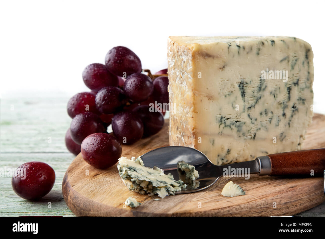 Stilton auf einem Käsebrett mit roten Trauben und Käse Löffel Stockfoto