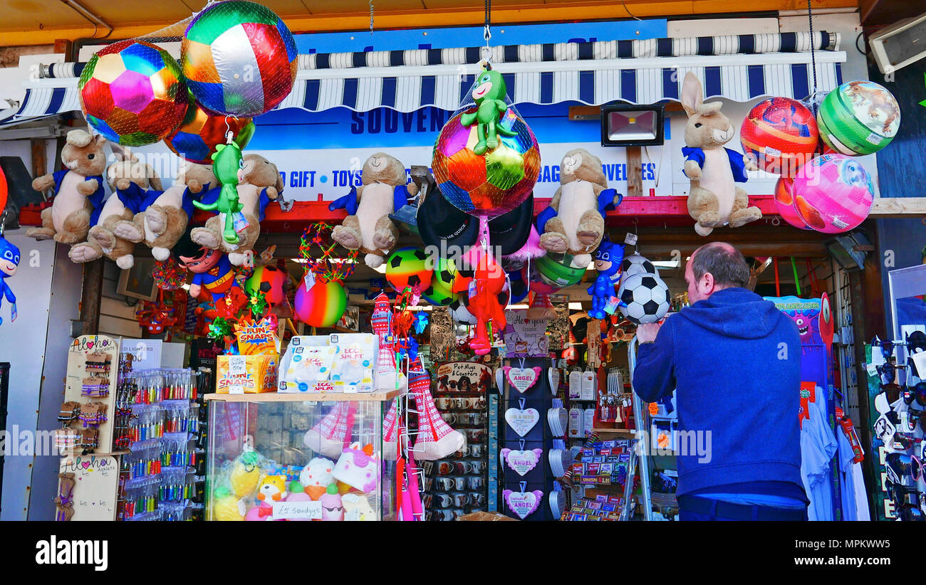 Mann auf Schritt Leitern Vermittlung von Spielzeug zum Verkauf im Seaside Shop bei Blackpool, Lancashire, Großbritannien, Stockfoto