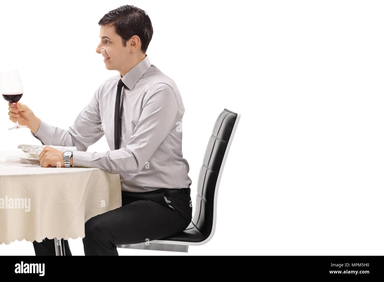 Junge Mann hält ein Glas Rotwein an einem Tisch im Restaurant auf weißem Hintergrund Stockfoto