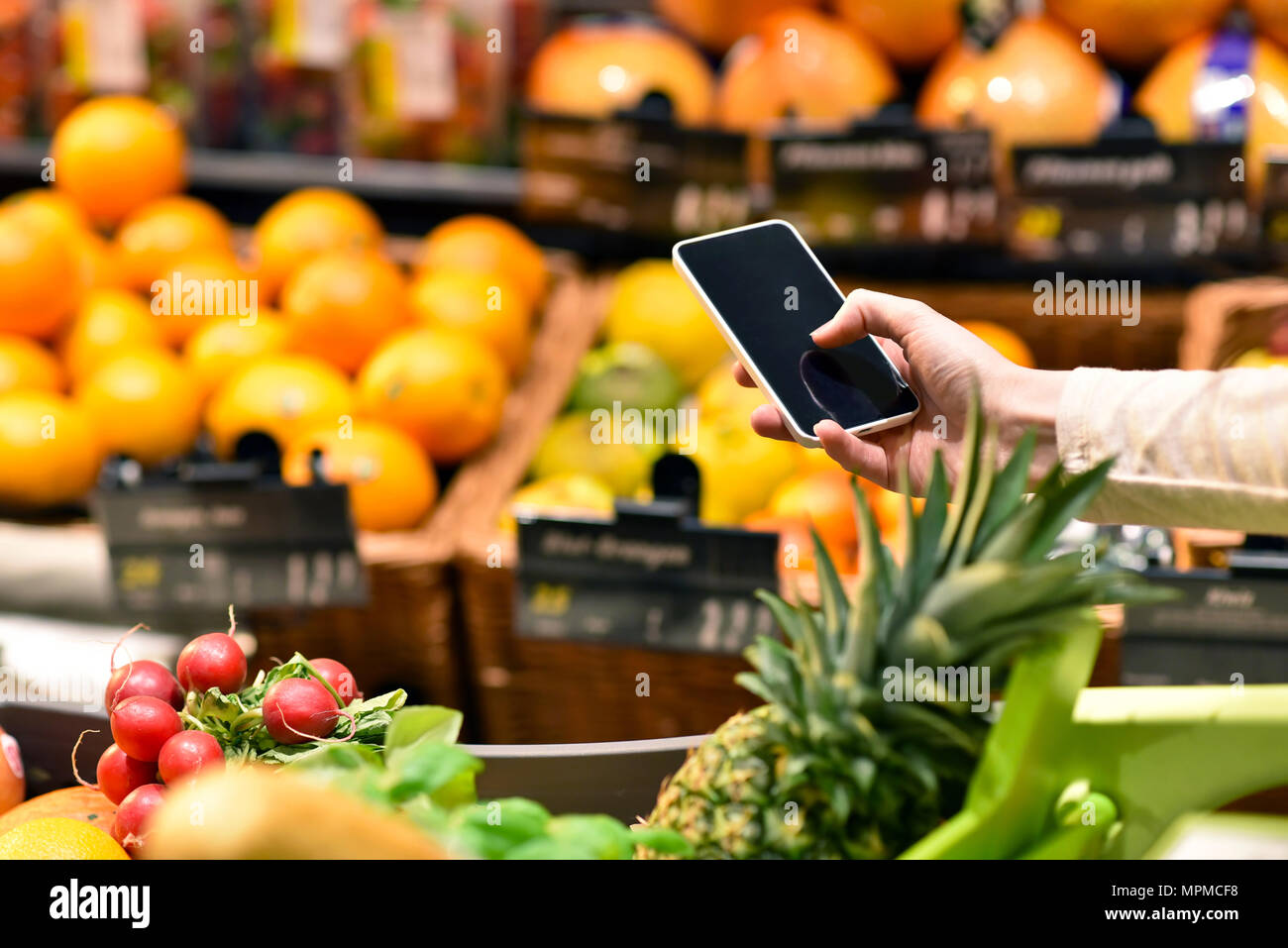 Einkauf im Supermarkt mit Smartphone - Preisvergleich und Informationen - - Kauf von frischem Obst und Gemüse Stockfoto