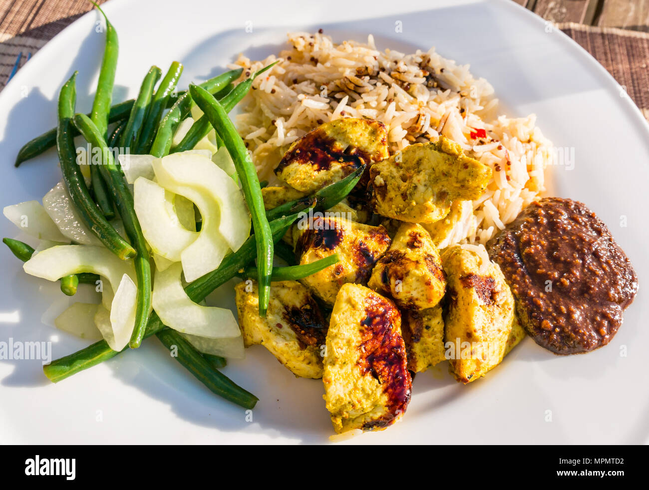 Indonesischen Mahlzeit weiß Teller Tisch serviert auf der Terrasse in der Sonne. Chicken Satay, Erdnuß-Sauce, kecap masin Sauce, Reis, Bohnen und Gurken Stockfoto