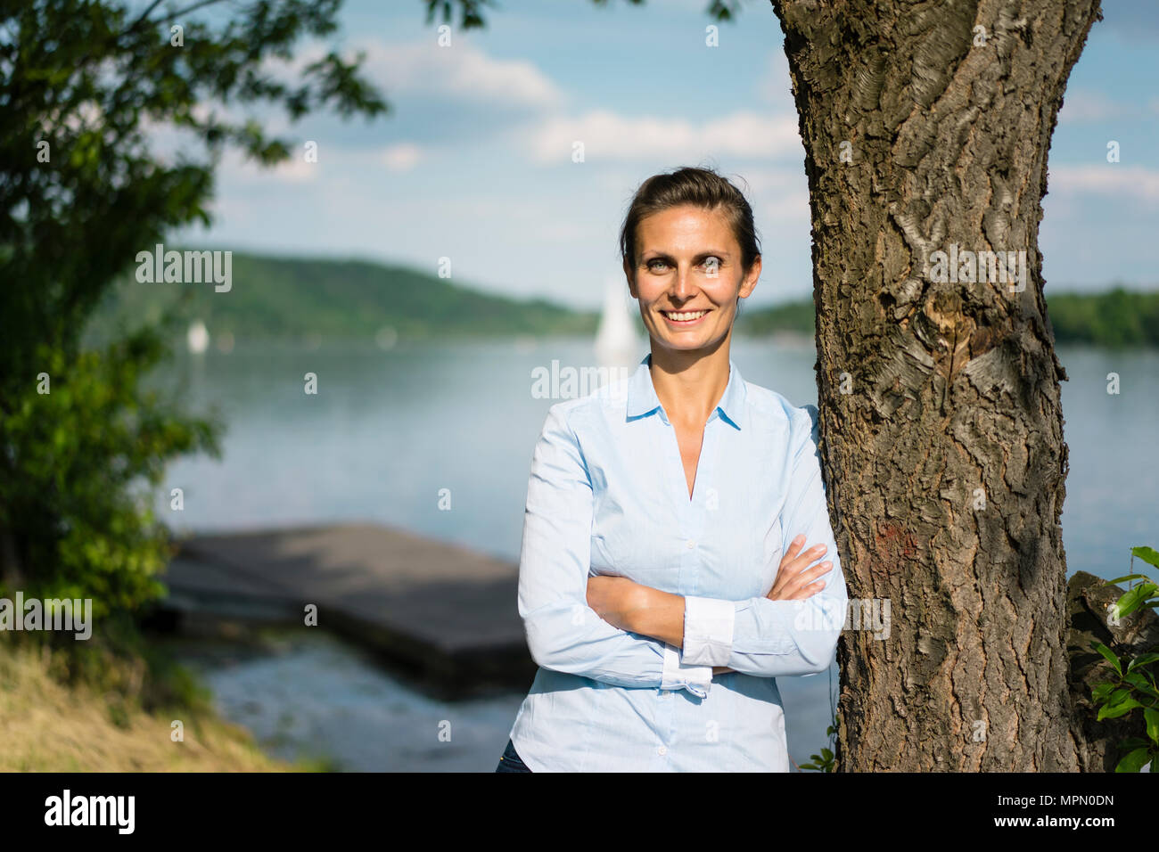 Porträt der lächelnde Frau lehnte sich an einem Baum an einem See Stockfoto