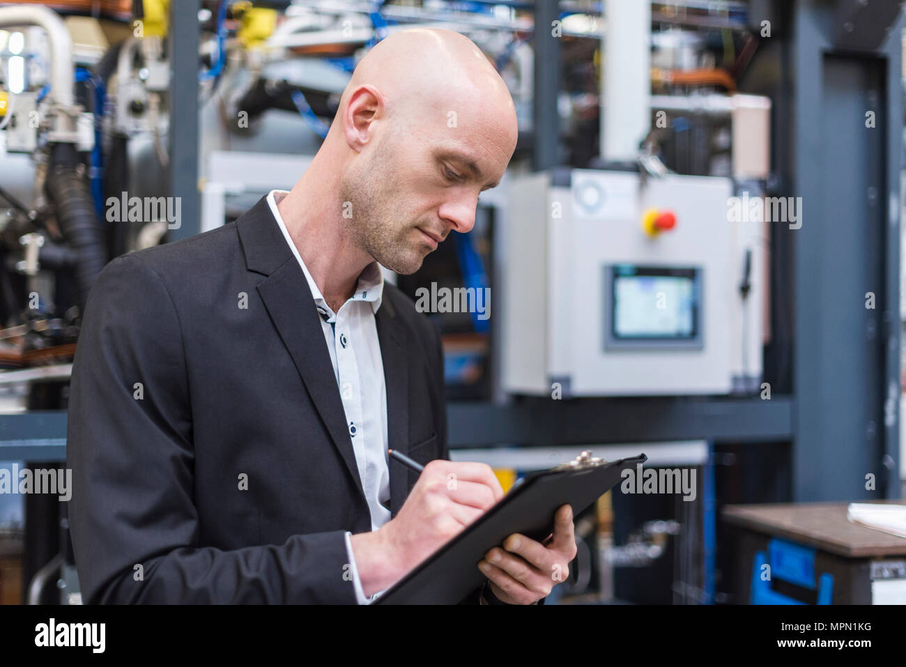 Unternehmer schriftlich über die Zwischenablage in der modernen Fabrik Stockfoto