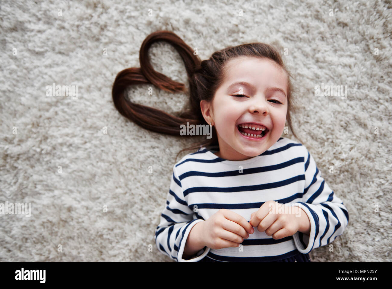 Portrait von Lachen kleines Mädchen liegt auf dem Teppich Stockfoto