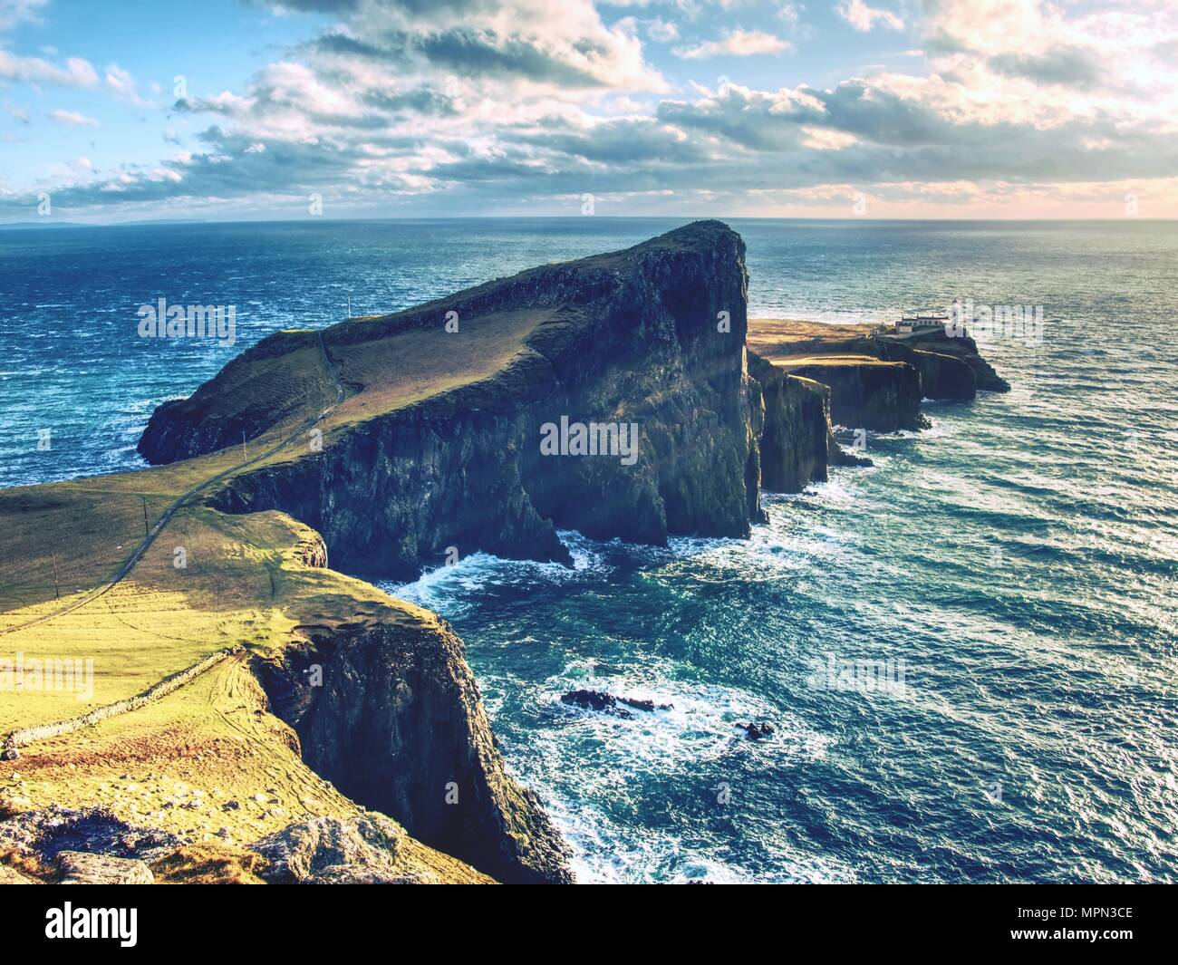 Der alte Leuchtturm am Ende der schmalen Landzunge. Scharfe felsige Klippe aganst zu schäumenden Ozean, Abend blauer Himmel. Stockfoto