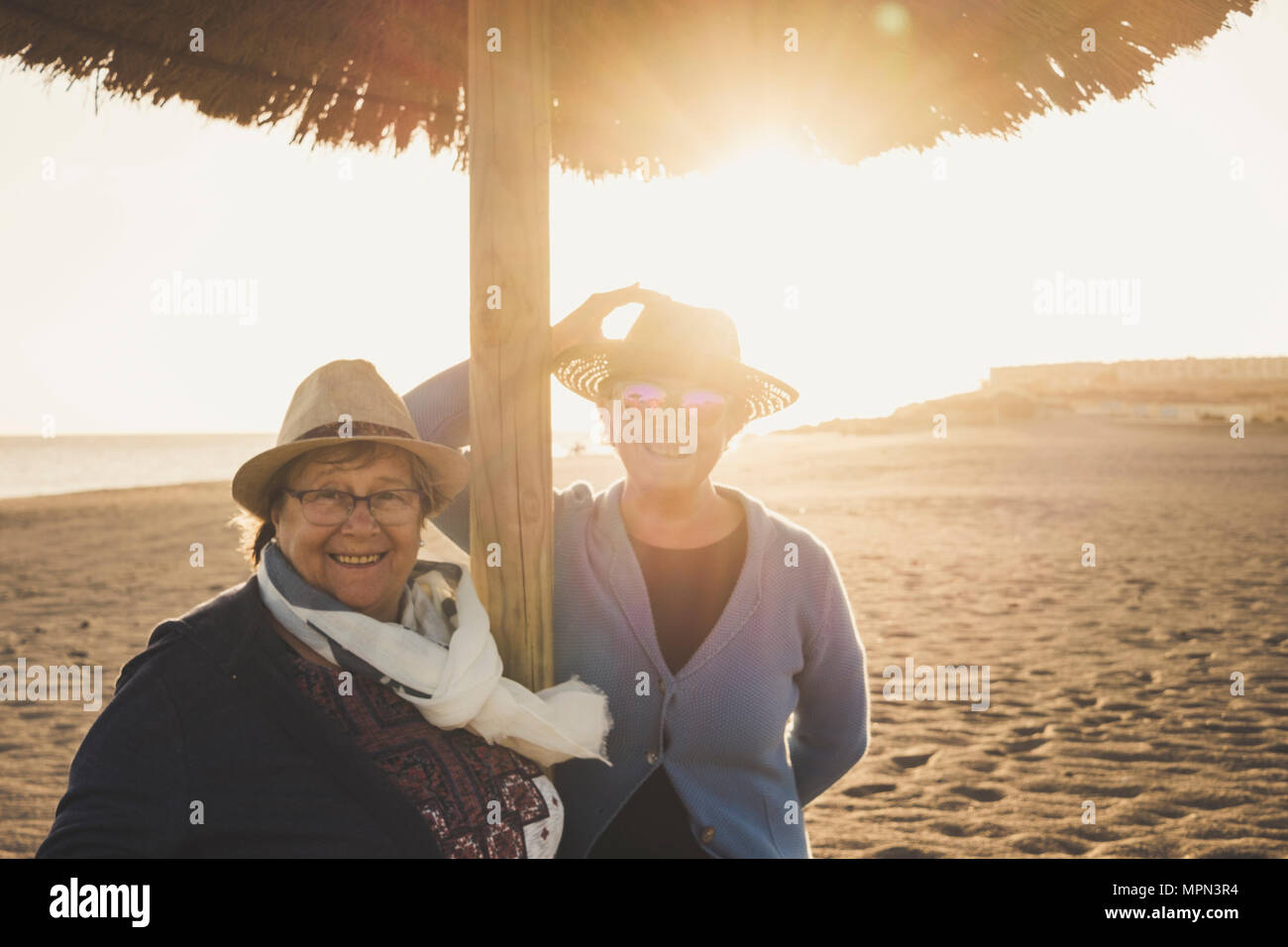 Paar weibliche Senioren im Alter am Strand bei Sonnenuntergang auf Teneriffa. Freizeitaktivitäten Konzept für 60 s Frauen mit Hüten und Hintergrundbeleuchtung. Warme Filter. Stockfoto