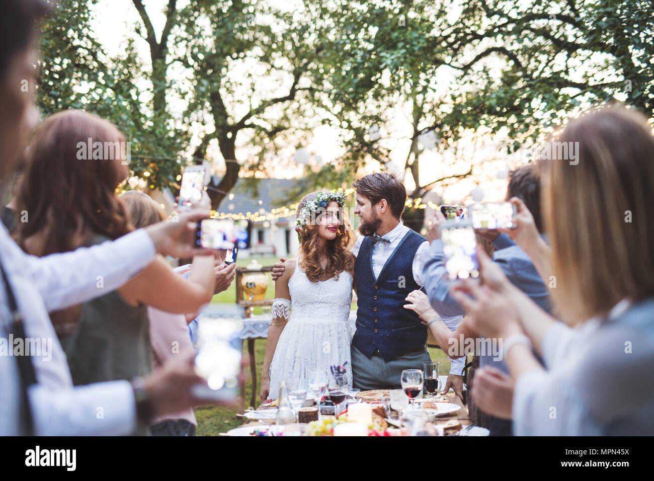 Gäste mit Smartphones unter Foto von Braut und Bräutigam bei der Hochzeit außerhalb. Stockfoto