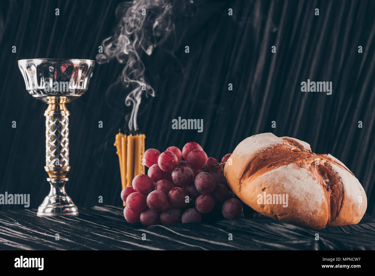 Brot, Trauben, Kerzen und Kelch auf dunklem Stoff für die Heilige Kommunion Stockfoto