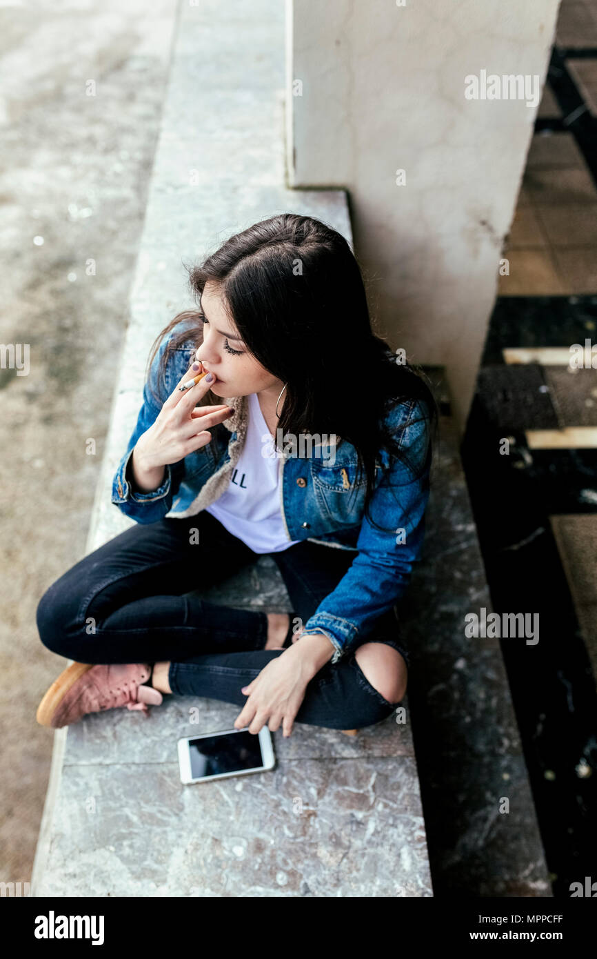 Junge Frau sitzt auf einer Wand das Rauchen einer Zigarette Stockfoto