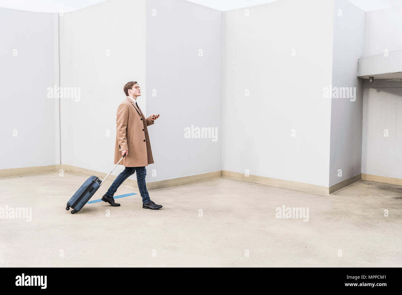 Geschäftsmann mit rollenden Koffer und Handy am Parkplatz Garage Stockfoto