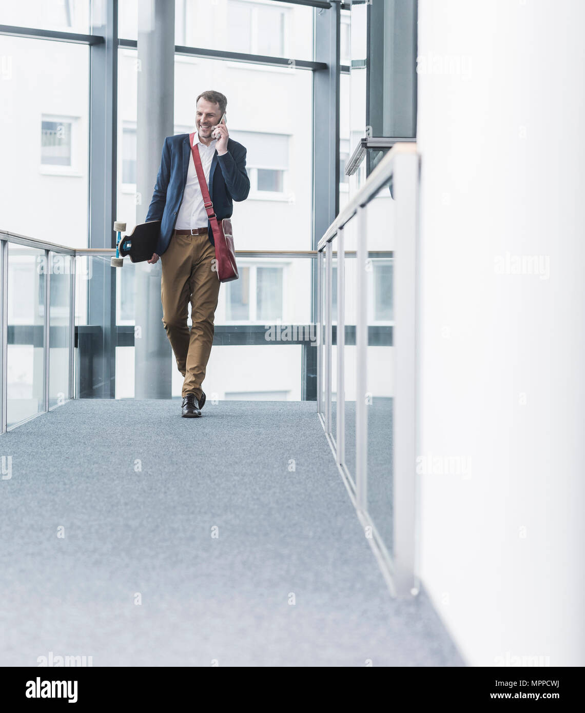 Lächelnd Geschäftsmann holding Skateboard und Gespräch am Handy Stockfoto