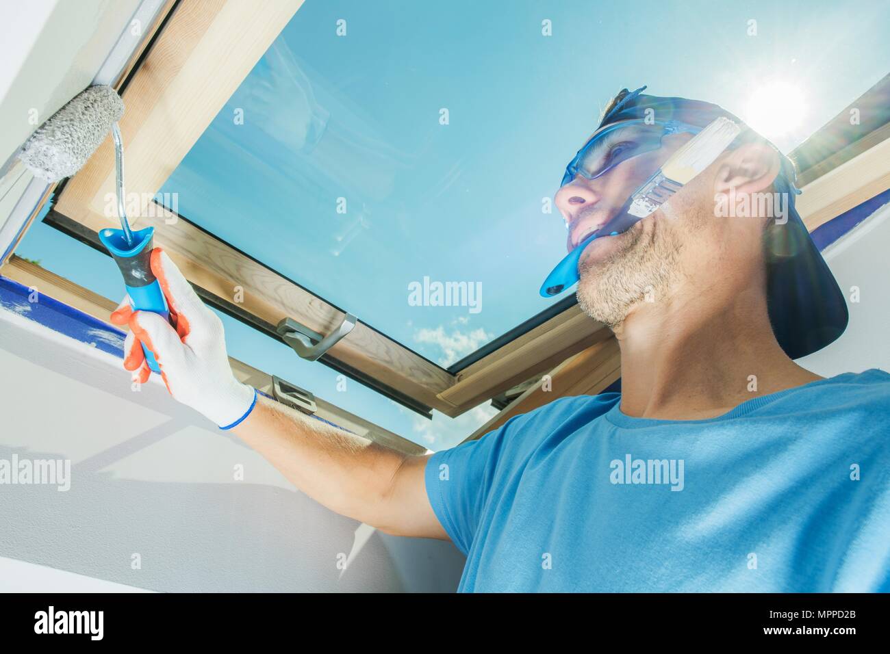 Zimmer Maler Multitasking. Kaukasische Bauarbeiter mit Pinsel im Mund Malerei Wände mit Walze. Stockfoto