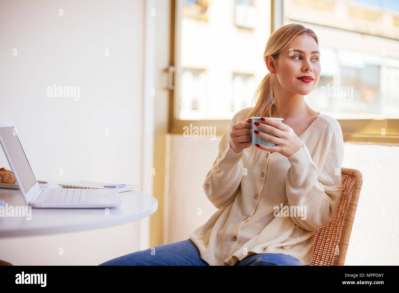 Blonde Frau mit Tasse Kaffee aus dem Fenster Stockfoto