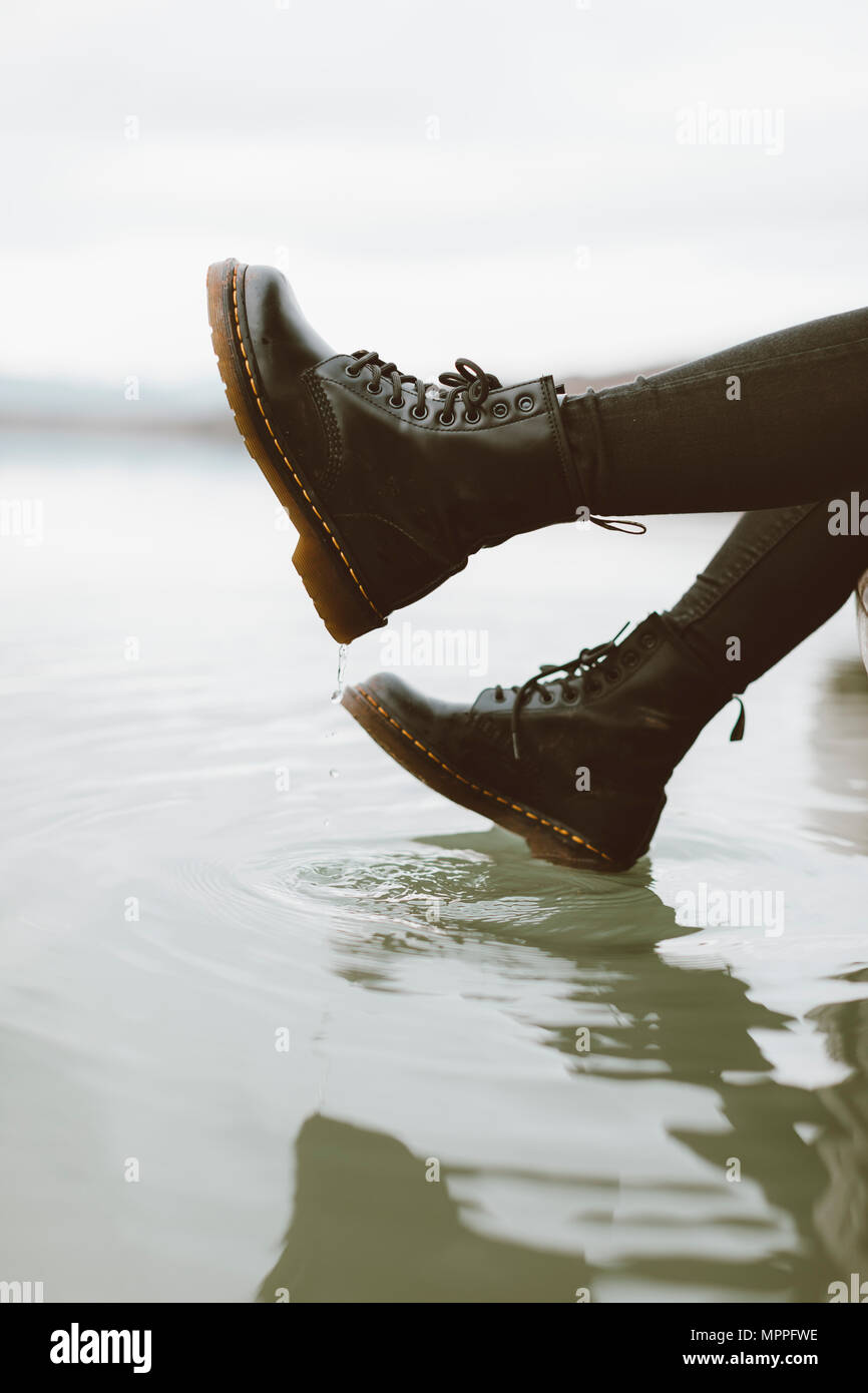 Frau mit schwarzen Stiefeln berühren Wasseroberfläche des Sees, Teilansicht Stockfoto