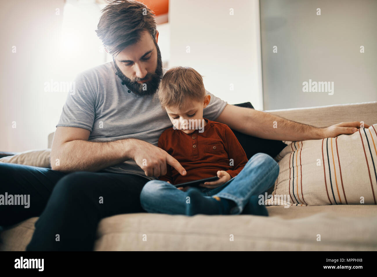 Vater und Sohn sitzen zusammen auf der Couch an Smartphone suchen Stockfoto