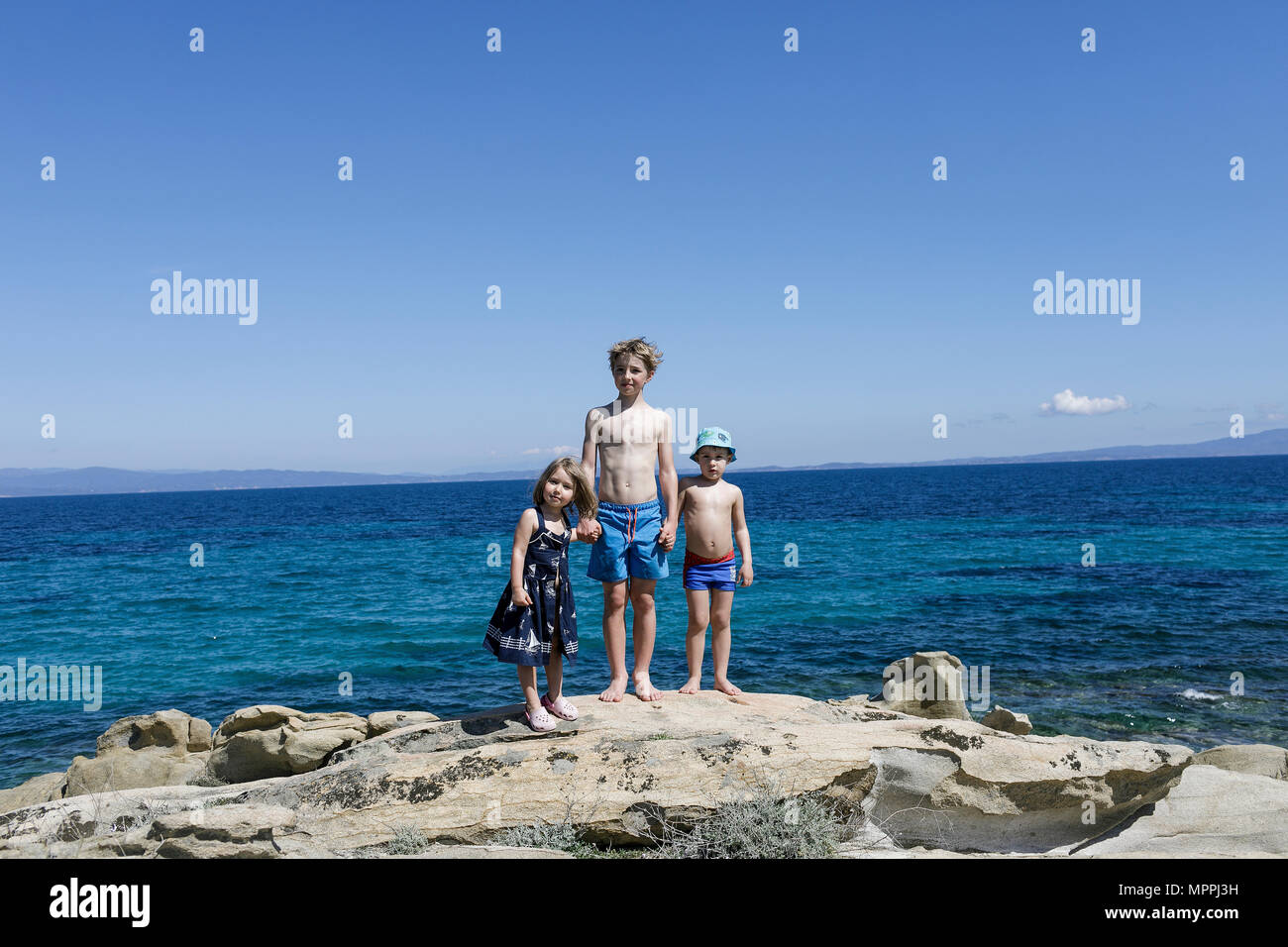 Griechenland, Chalkidiki, drei Kinder stamnding Hand in Hand auf den Felsen am Meer. Stockfoto