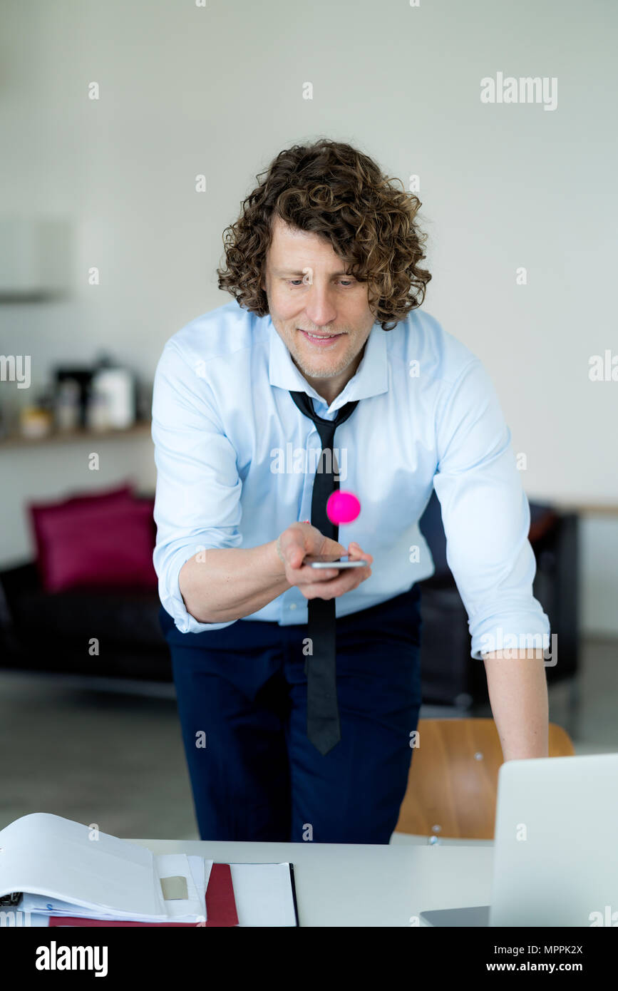 Geschäftsmann spielen Ping pong mit einem Ball und sein Handy Stockfoto