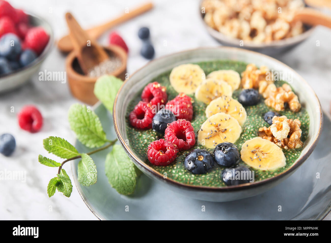 Buddha Schüssel grünem Chia Pudding mit Bananenscheiben, Blaubeeren, Himbeeren und Walnüsse Stockfoto