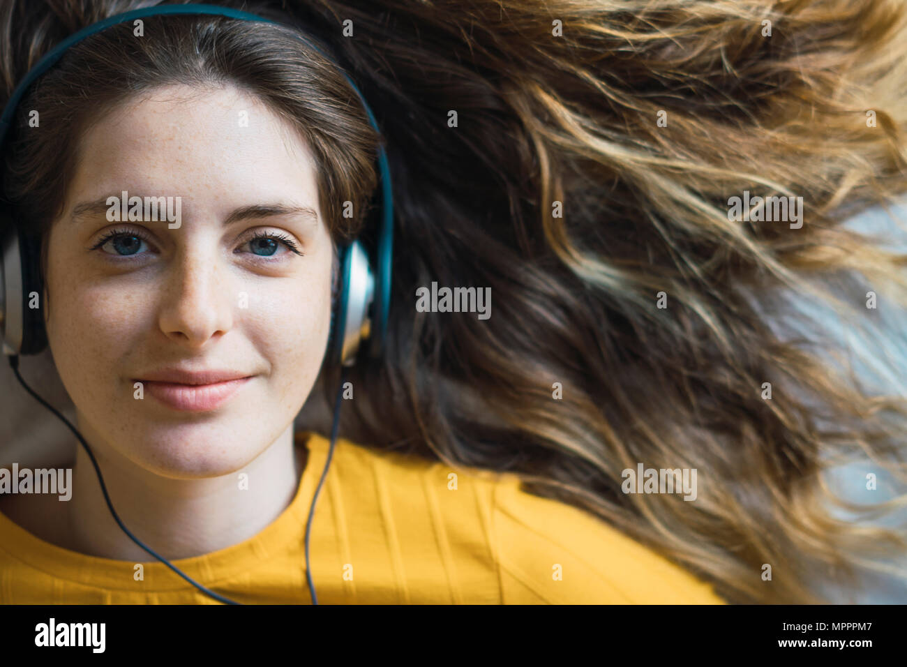 Portrait von lächelnden jungen Frau mit Kopfhörern liegend auf Bett Stockfoto
