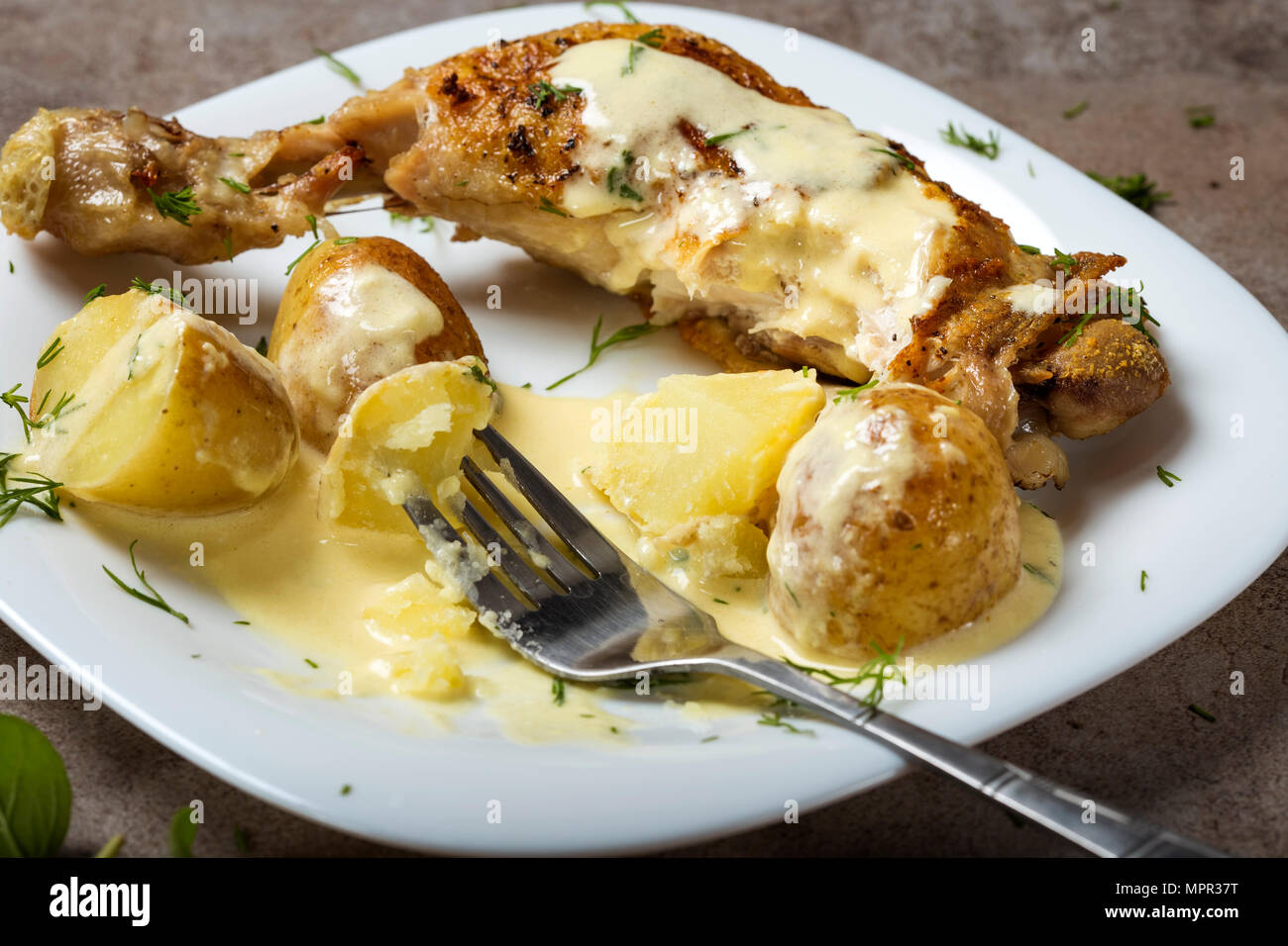 Ein gebratenes Huhn Bein mit neuen Kartoffeln und saure Sahne Soße auf einer weißen Platte Stockfoto