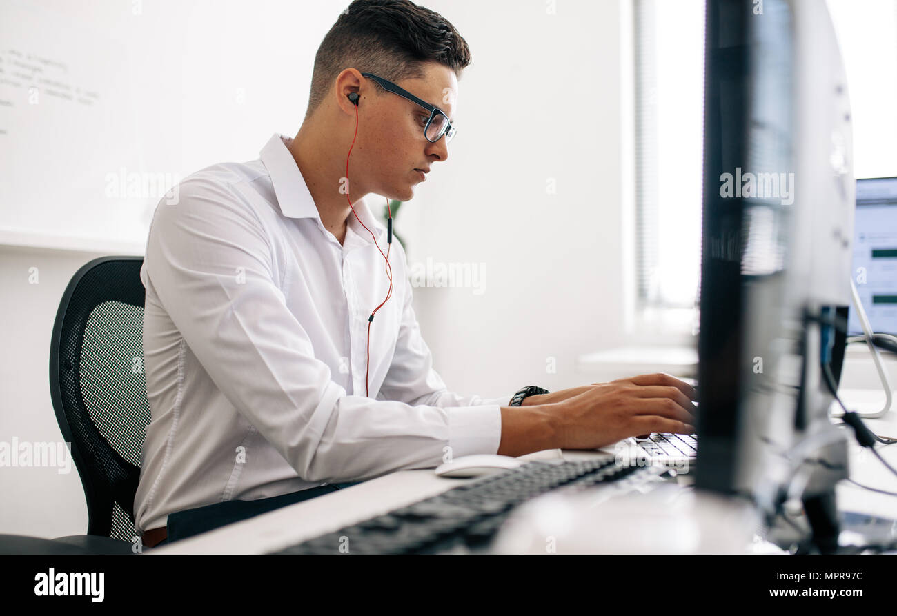 Software Entwickler sitzt in seinem Büro Schreibtisch arbeiten am Laptop das Tragen von Kopfhörern. Mann mit Brille arbeiten am Laptop im Büro. Stockfoto